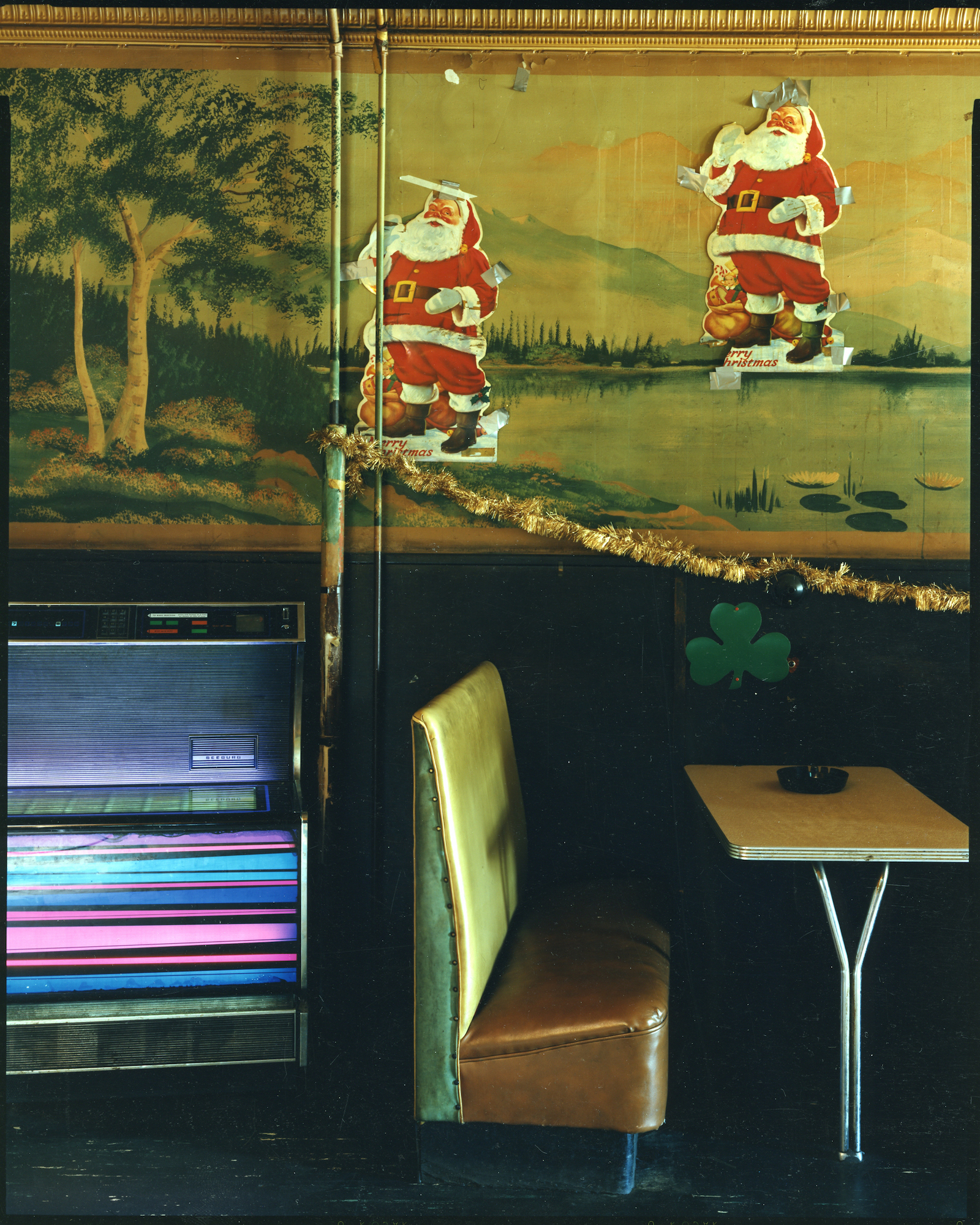 Diner booth with 2 Santa Claus figures above table, 1985